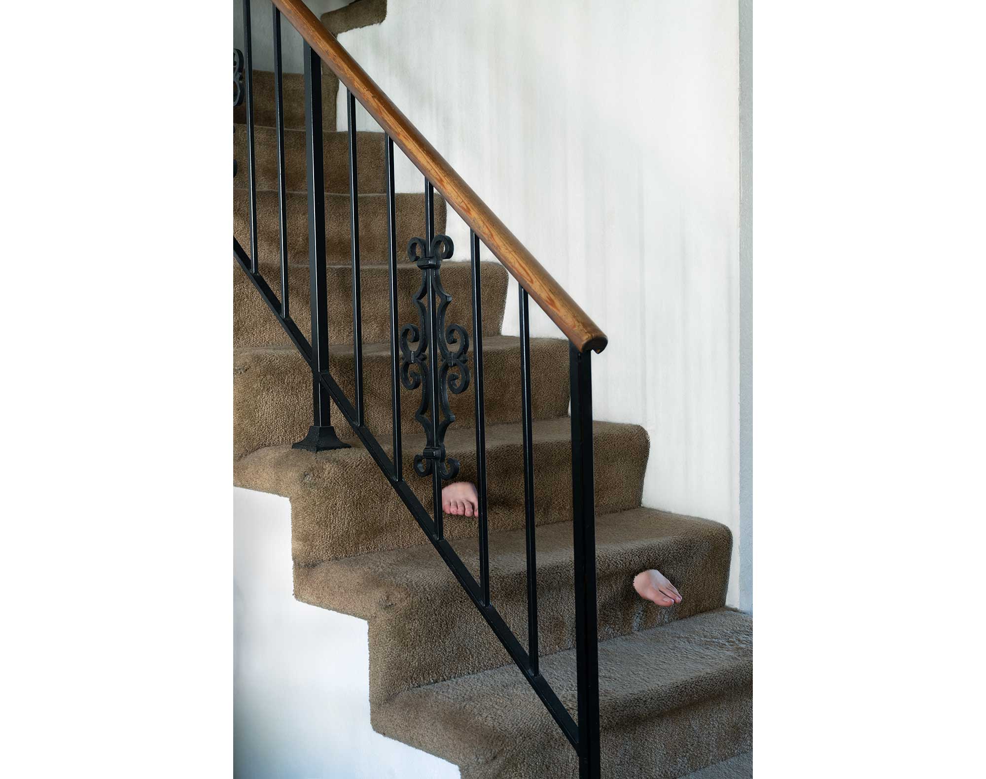 Two feet descend stairs with no body attached. The feet are shown emerging from the carpet on the front of the stair steps.