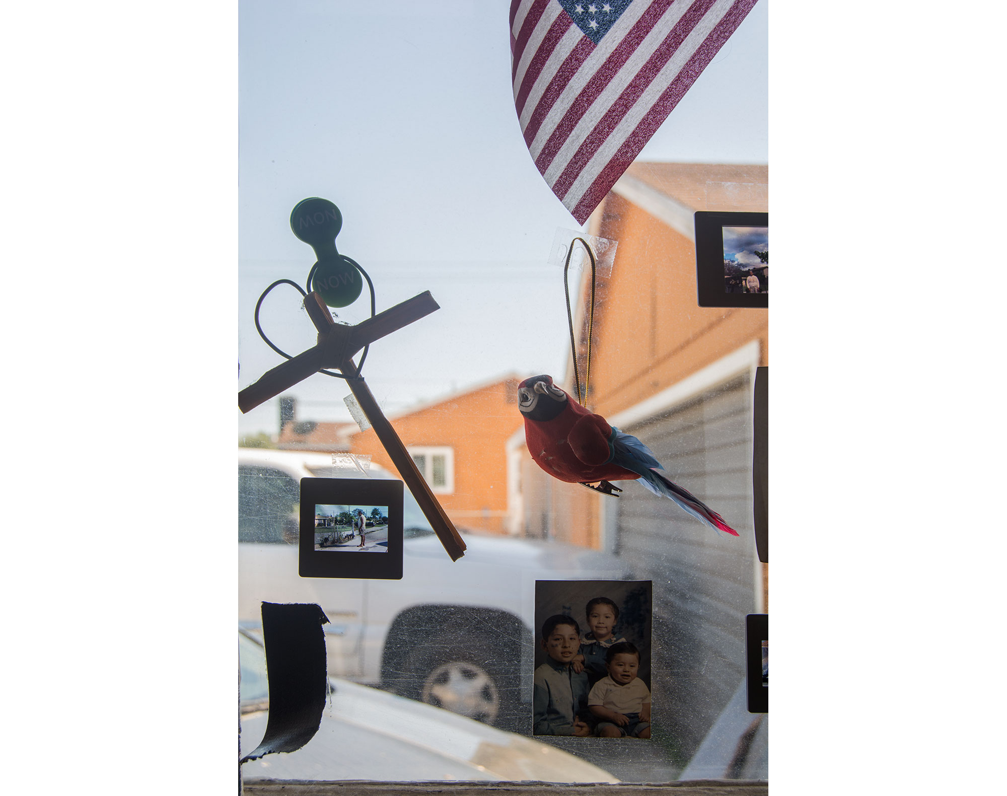 A close up shot of the first piece that focuses on the cross made of palm leaves, red parrot, 35mm slide, and part of the American flag. There is also a wallet sized photograph of my brother, sister, and I